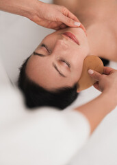 Fototapeta na wymiar Crop professional cosmetician using gua sha tool during face massage