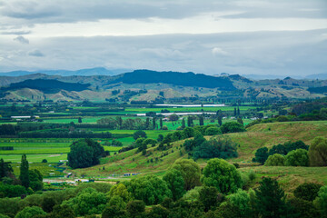 Fototapeta na wymiar Aerial view over lush green farmland and distand mountain range under cloudy sky. Iconic New Zealand Landscape. Greys Hill Lookout, Gisborne, North Island, New Zealand