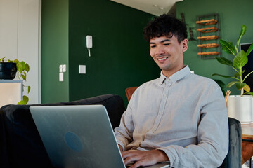 Young multiracial man wearing shirt smiling while using laptop on sofa at home