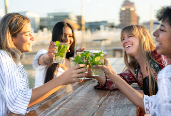 Multiethnic friends raising their mojitos in celebration while enjoying a day at the beach. The...