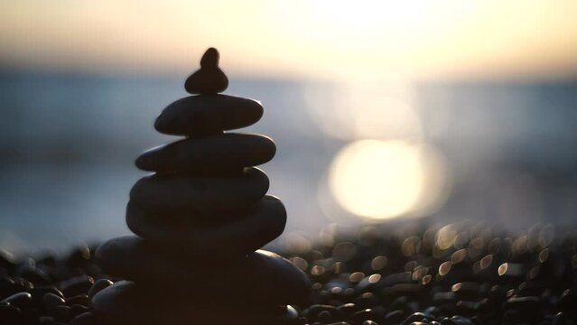 Balanced rock pyramid on pebbles beach. Golden sea bokeh on background. Selective focus, zen stones on sea beach, meditation, spa, harmony, calm, balance concept.