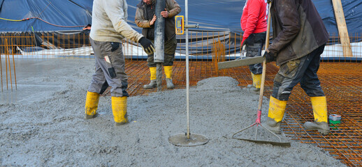 Bauarbeiter gießen die Bodenplatte eines Einfamilienhaus-Neubaus über der Baustahlmatte mit der...