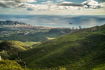 view from Mount Bernia on the trees and valley and apartment buildings of the city of Benidorm and Serra Gelada