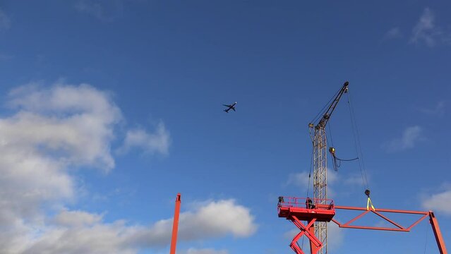 Plane flies over the construction site with a crane, metal structures, workers on a scissor lift.