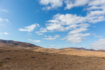 Fototapeta na wymiar amazing desert landscape with blue sky and white clouds with mountain range in the background. Fuerteventura, Canary Islands, Spain