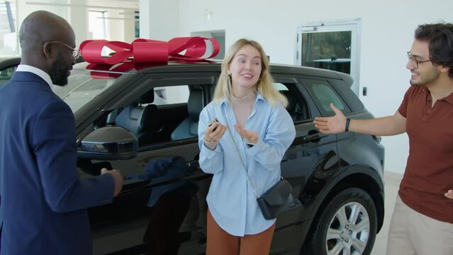 Happy young Caucasian woman getting new crossover car as a gift for her birthday, medium long shot