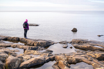 Fototapeta na wymiar Woman standing on a rocky beach, looking at the sea. Fäboda, Jakobstad/Pietarsaari, Finland.