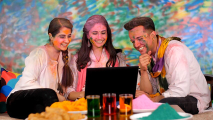 Beautiful young sisters and brother wishing happy Holi over video call - Relationships  pretty faces . Friends doing an online call via laptop - colored faces  dress in colors