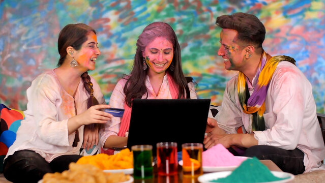 Indian Friends Covered With Colors And Shopping Online At-home - Internet Use  Online Payment. Beautiful Sisters And Handsome Young Male Filling Debit Card Details To Purchase Groceries On Holi - S...