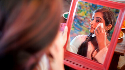 An attractive girl with braided hair taking off Holi colors from her face - skin care . A pretty...
