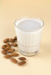Almond milk in glass on a beige background and almond kernels. Lactose free nut milk.