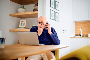 Middle age businessman sitting at home and using laptop and mobile phone for work