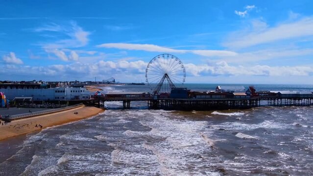 pier overhead view. Birds flying on the Ferris wheel and the pier. Waves crashing on the shore in the blue sea