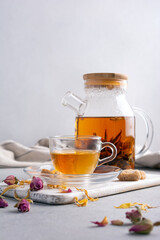 Glass teapot of hot fragrant craft blossom tea with cup and dry rose bud, sugar