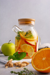 Glass teapot of hot healthy sweet fruit tea with fresh ripe citrus, apples, mint and thyme