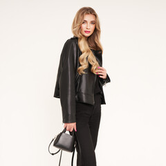 Fototapeta premium Young blonde woman in black leather jacket and black jeans. Girl posing on a white background. Jewelry and hairstyle. Fashion photo