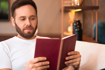 focused man reading book and sitting in armchair at home