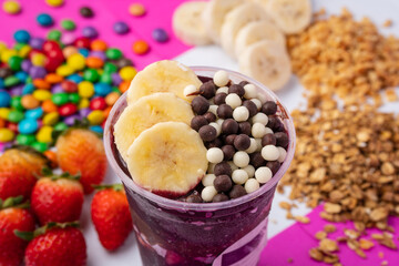close up of acai or açaí cup with topping chocolate ball and banana in colorful background