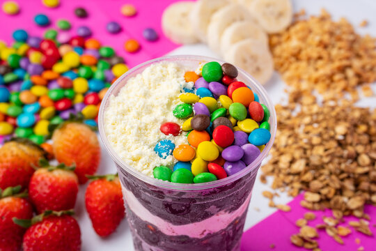 close up of frozen acai or açaí cup with topping confetti and powdered milk in colorful background