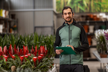 A man working in a houseplant nursery is doing the inventory and posing for the camera.