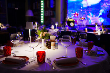 a table with a white tablecloth, glasses, crockery and decor in dark restaurant