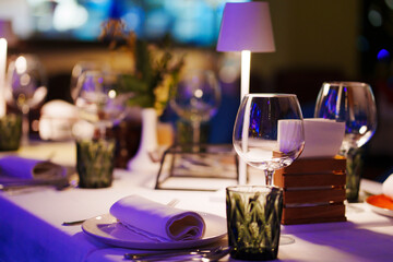 a table with a white tablecloth, glasses, crockery and decor in dark restaurant