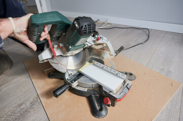 Close up of male worker using electric circular saw with abrasive disc while preparing material for construction works. Man cutting plank with hand-held circular power saw on the floor in apartment.