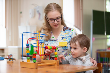 A psychologist is working with a small child, showing a children's wooden educational toy-maze and...