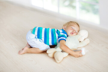 Baby sleeping on floor with toy and milk bottle.