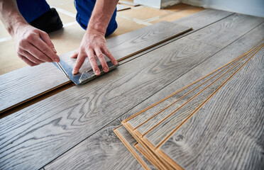 Man preparing laminate plank for floor installation in apartment under renovation. Close up of male...
