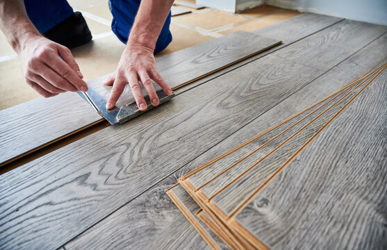 Man Preparing Laminate Plank For Floor Installation In Apartment Under Renovation. Close Up Of Male Worker Using Metal Construction Ruler And Pen While Drawing Line On Laminate Flooring Board.