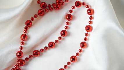 Red  necklace on the white, soft, and delicate with shine, folds,  elegant silk background