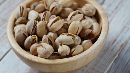 Bowl of whole dry pistachio nuts on wooden table