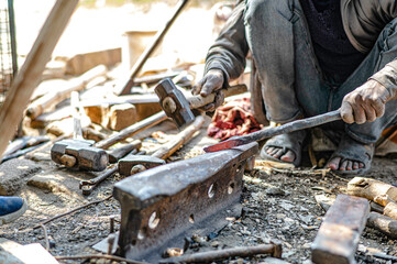 A blacksmith is forging iron rods into tools. Equipment at a roadside blacksmith shop in India