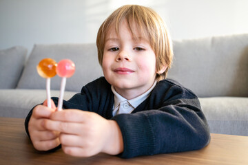 Little toddler child, blond boy, licking lollipop at home