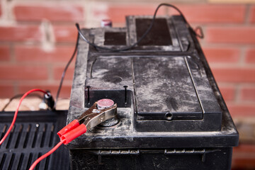Car battery is connected to charger with alligator clips.