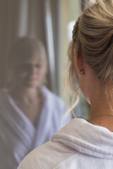 Girl in a white bathrobe watching her reflexion in a window - concept  for wellness, spa, therapy