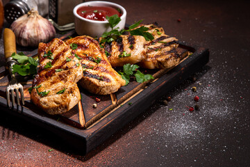 American bbq food concept. Grilled barbeque pork meat steaks with tomato bbq sauce, spices and greens, on cutting board, dark background top view copy space 