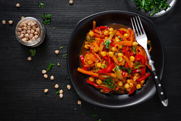 Vegetable stew of chickpeas, carrot, sweet peppers, onions, garlic and tomato sauce with lemon on the dark table. Oriental cuisine. Top view