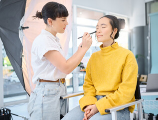 Beauty, makeup artist and model doing makeup on a for a creative photoshoot in a studio. Cosmetics, art and beautician preparing a young Asian woman with a cosmetic routine for a photography job.