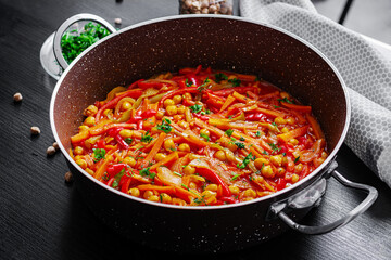 Vegetable stew of chickpeas, carrot, sweet peppers, onions, garlic and tomato sauce with lemon on the dark table. Oriental cuisine.