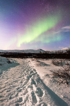 imagen de un paisaje nocturno nevado con auroras boreales en el cielo y todo iluminado por la luz de la luna en Islandia