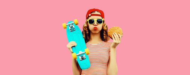 Portrait of stylish young woman with burger fast food and skateboard wearing baseball cap, sunglasses on pink background