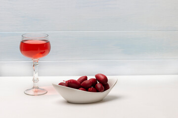 A glass of rose wine and burgundy olives in a white bowl.