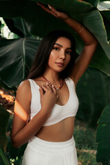 Portrait of a beautiful Asian woman with long hair standing in a tropical garden and looking at the camera.