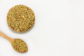 Small round grains of natural green lentils in a decorative plate and in a wooden spoon on a white background