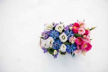 Top view of bright and colorful bouquet of fresh spring flowers: pink tulips, blue hyacinthes, white eustomas in box on white snowy background. Copy space