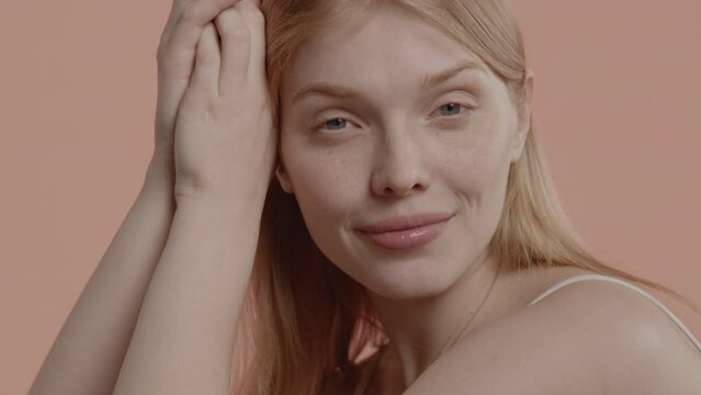 Beautiful young woman with no makeup gently smiles against neutral brown pastel background. Studio shot, soft lighting