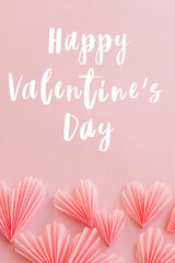 Fototapeta na wymiar Happy valentines day text on cute pink hearts flat lay on pink paper background. Modern Valentines day greeting card. Handwritten sign. Heart border