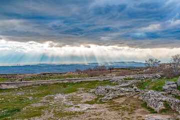 Groups of sunburst rays burst through the smoky blue Turkey clouds lighting up patches of hillside near Pamukkale Turkey